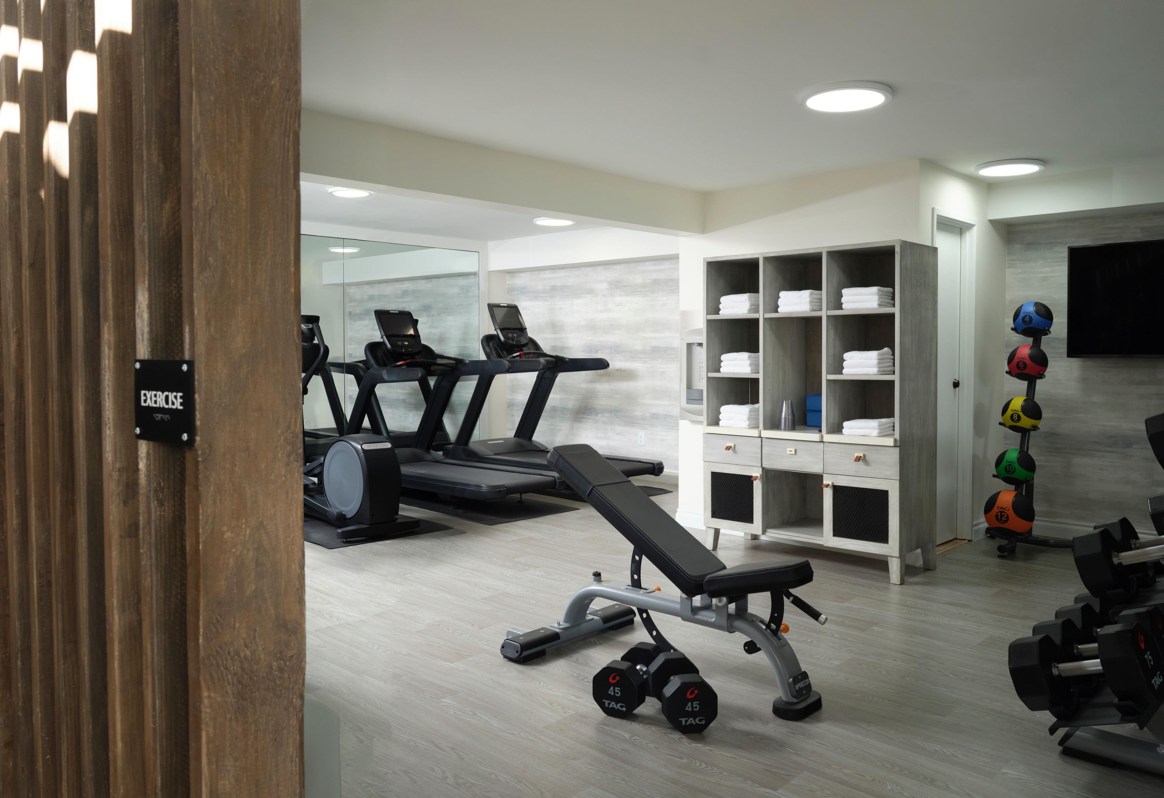 Un gimnasio con cintas de correr, banco, mancuernas y un armario.