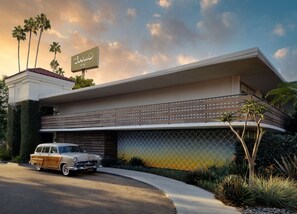 Un hotel moderno con techo plano, un cartel grande y un coche clásico estacionado al frente.