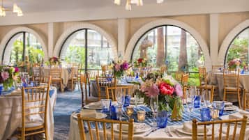 Une salle de banquet avec des tables rondes, des chaises en bois et des centres de table floraux.