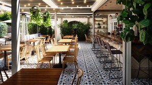 Un restaurante con mesas y sillas de madera, piso estampado, plantas colgantes y una zona de bar.