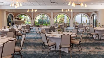 A banquet hall with round tables, chairs, and overhead lighting.