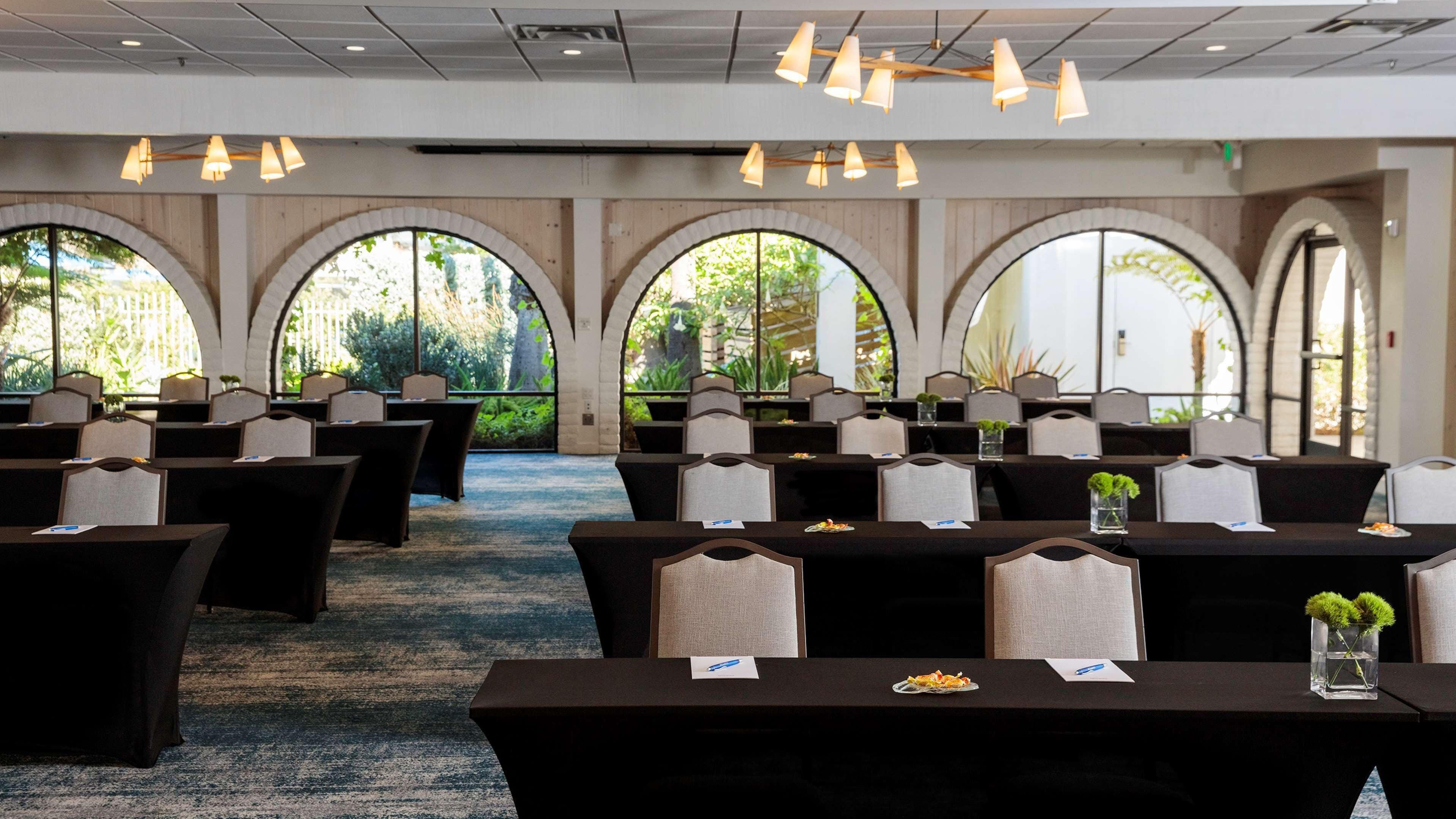 A conference room with tables and chairs, large arched windows, and hanging lights.