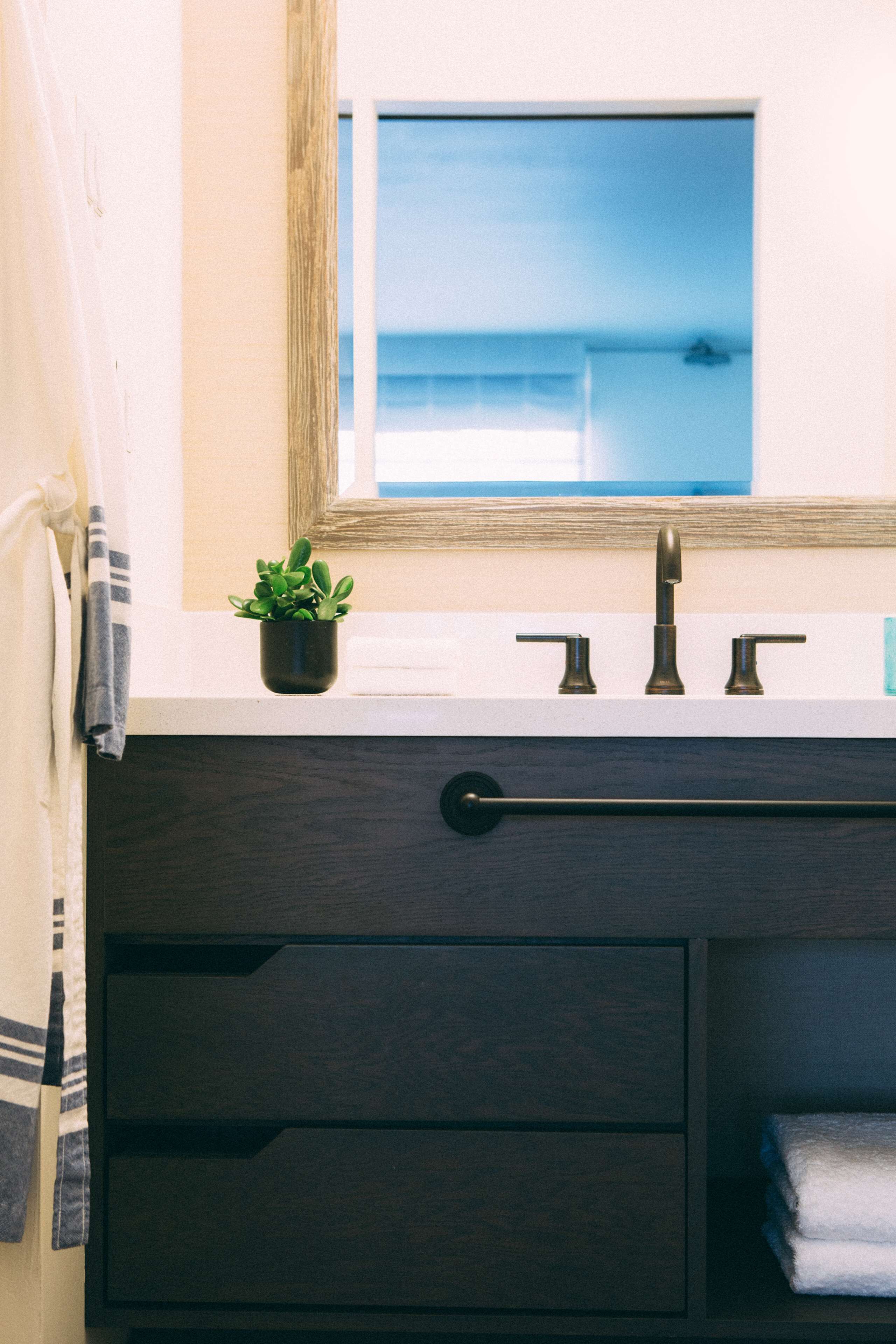Un tocador de baño con espejo, una pequeña planta en maceta y una toalla.