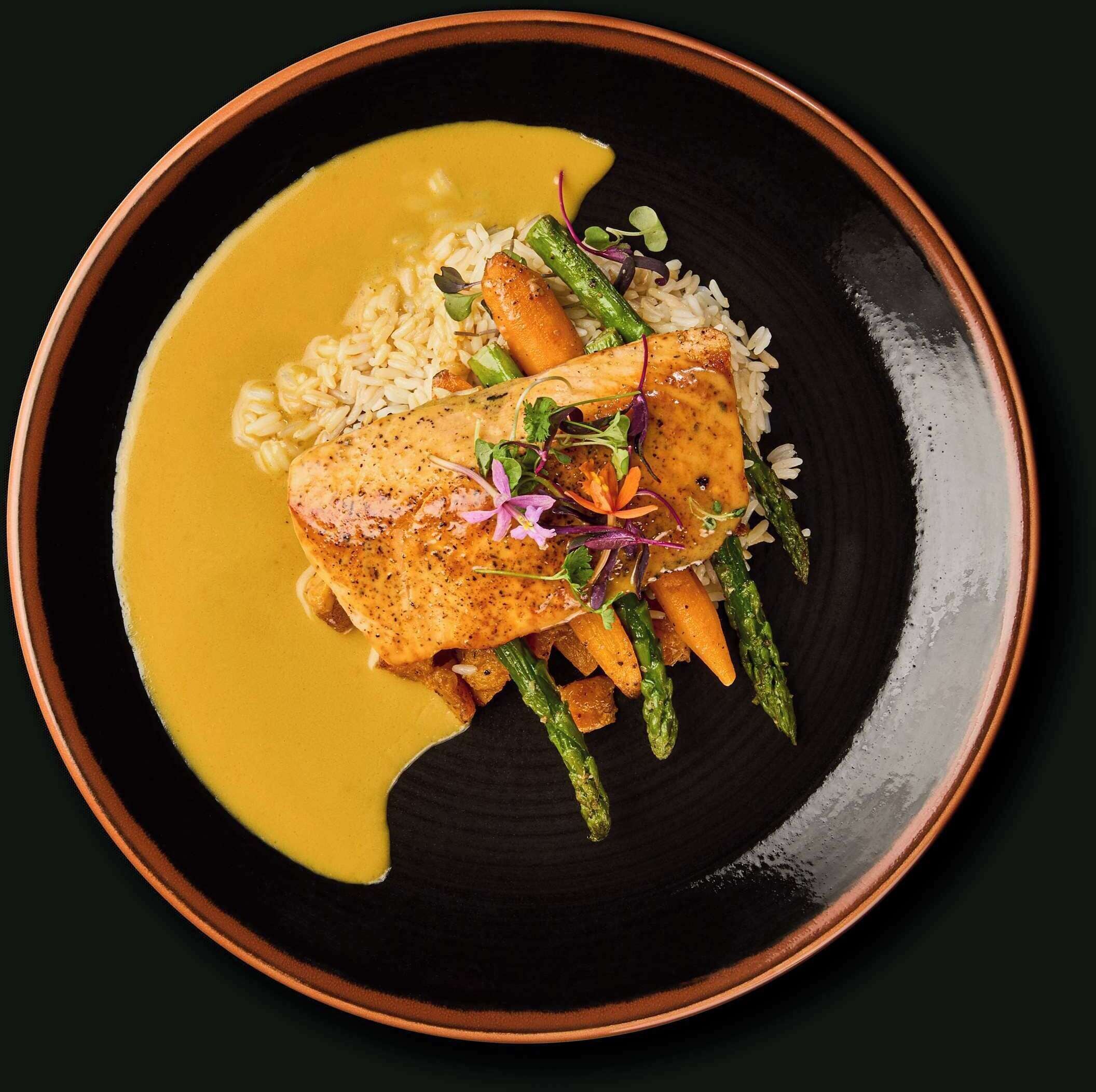 En tallerken med laks, asparges og ris, serveret med en gul sauce.