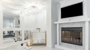 A modern bathroom with a large mirror, a freestanding bathtub, a vanity with a gold cart, and a fireplace. - The Burgundy Hotel, Tapestry Collection by Hilton (Little Rock)