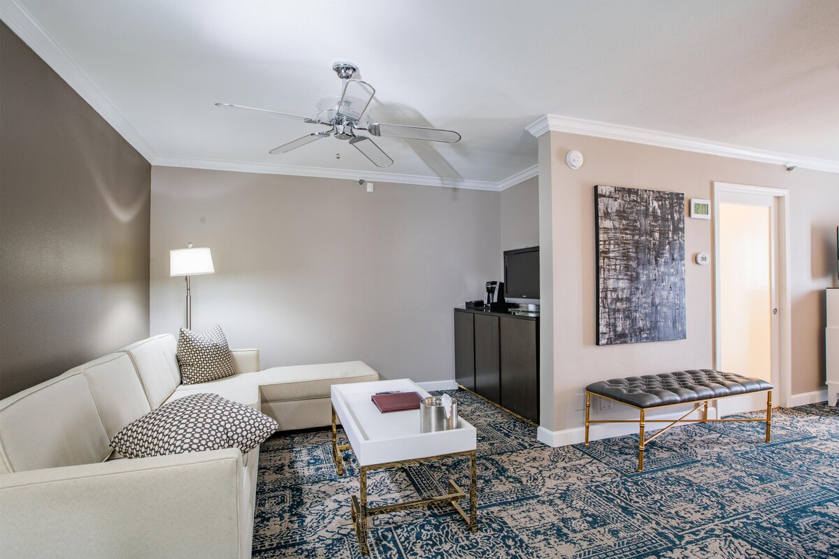 A modern living room with a ceiling fan, a sofa, a coffee table, a television, and a patterned rug.