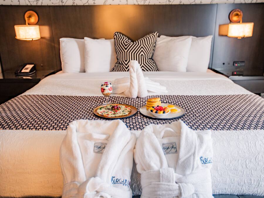 A neatly made bed with a patterned bedspread, two bedside tables with lamps, a bedside phone, and a tray with breakfast items.