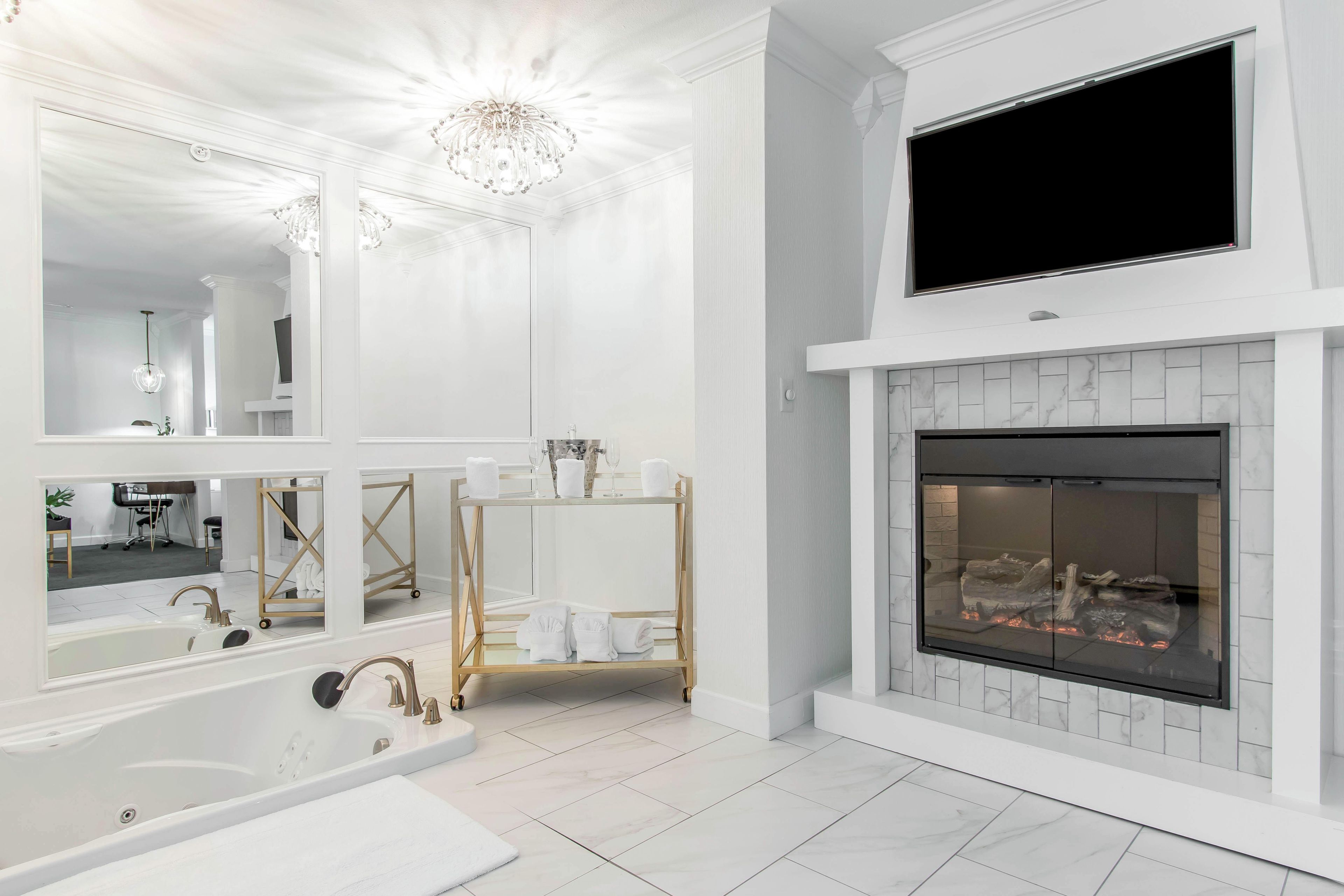 A modern bathroom with a large mirror, a bathtub, a vanity with a sink, and a fireplace.