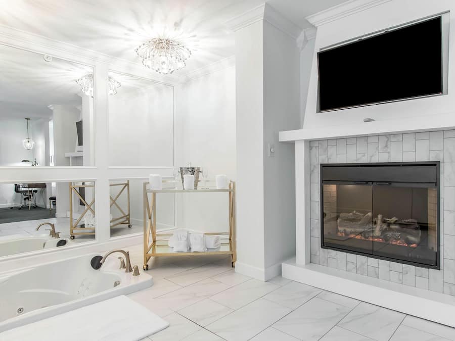A modern bathroom with a large mirror, a bathtub, a vanity with a sink, and a fireplace.