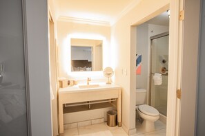 A bathroom with a sink, mirror, toilet, and glass-enclosed shower. - The Burgundy Hotel, Tapestry Collection by Hilton (Little Rock)