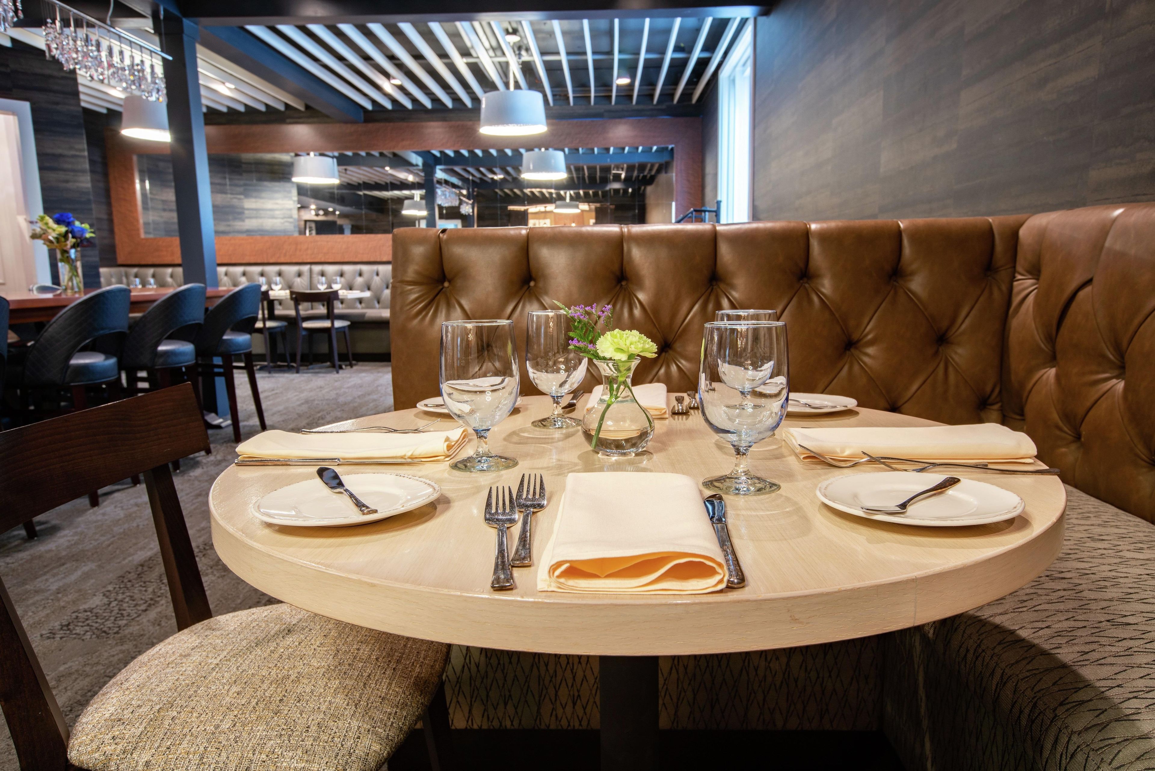 A round dining table with a brown leather booth in the center, set with plates, cutlery, and wine glasses.