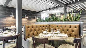 A restaurant interior with a central booth seating, round tables, and a decorative plant arrangement.
