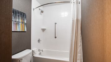 A bathroom with a white bathtub, a shower with a curved grab bar, a toilet, and a towel rack.