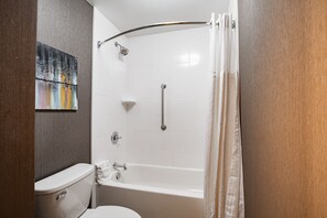 A bathroom with a white bathtub, a shower with a curved grab bar, a toilet, and a towel rack. - The Burgundy Hotel, Tapestry Collection by Hilton (Little Rock)