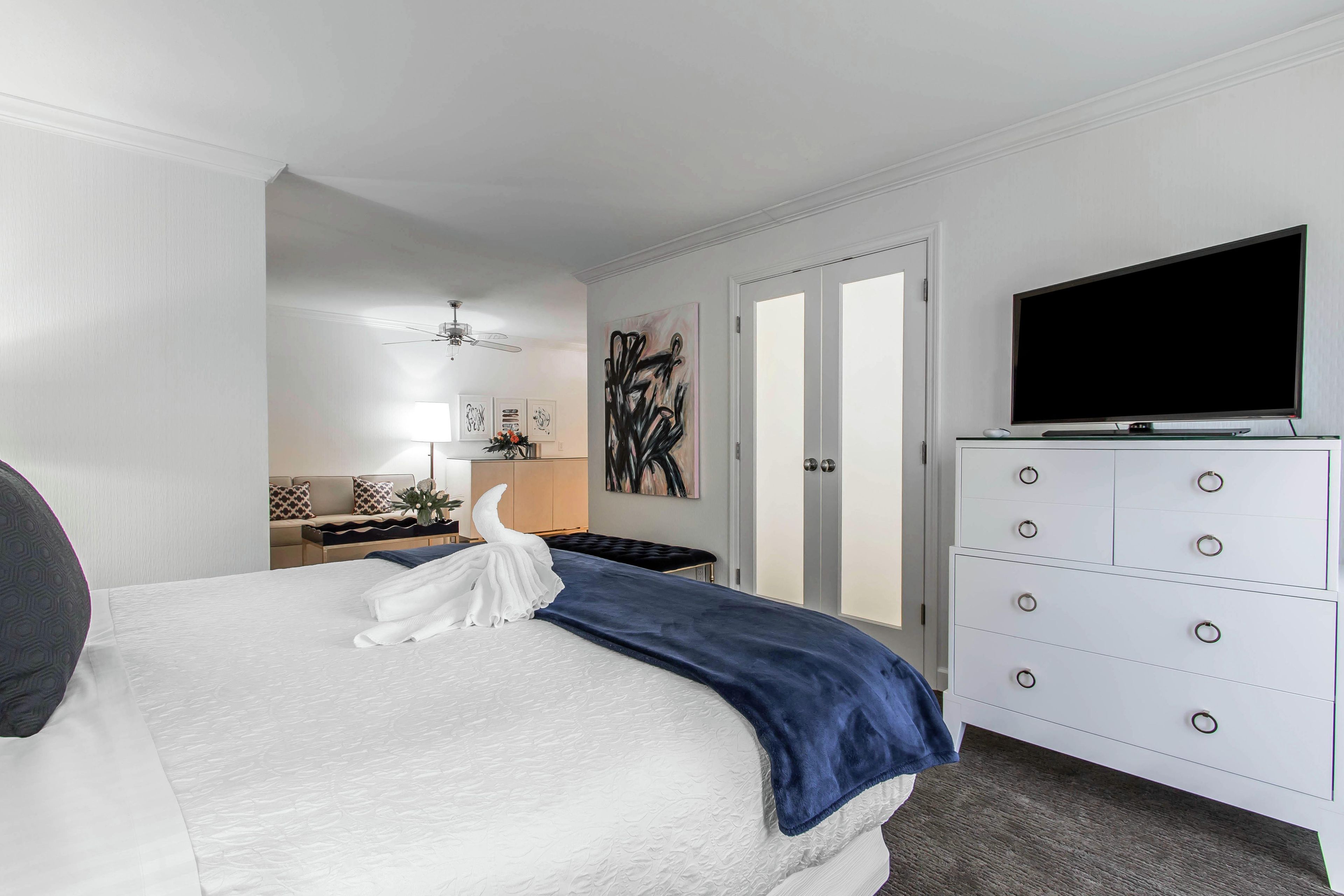 A hotel room with a bed, a dresser, a television, and a painting on the wall.