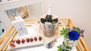 A tray with a bottle of champagne, a glass, a plate with chocolate-covered strawberries, and a vase with a blue rose. - The Burgundy Hotel, Tapestry Collection by Hilton (Little Rock)