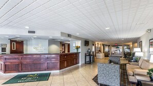 A hotel lobby with a reception desk, a seating area with a couch and chairs, and a tiled floor. - Quality Inn University (Lansing)