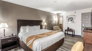 A hotel room with a large bed, bedside lamps, a desk, a chair, and a framed artwork on the wall.