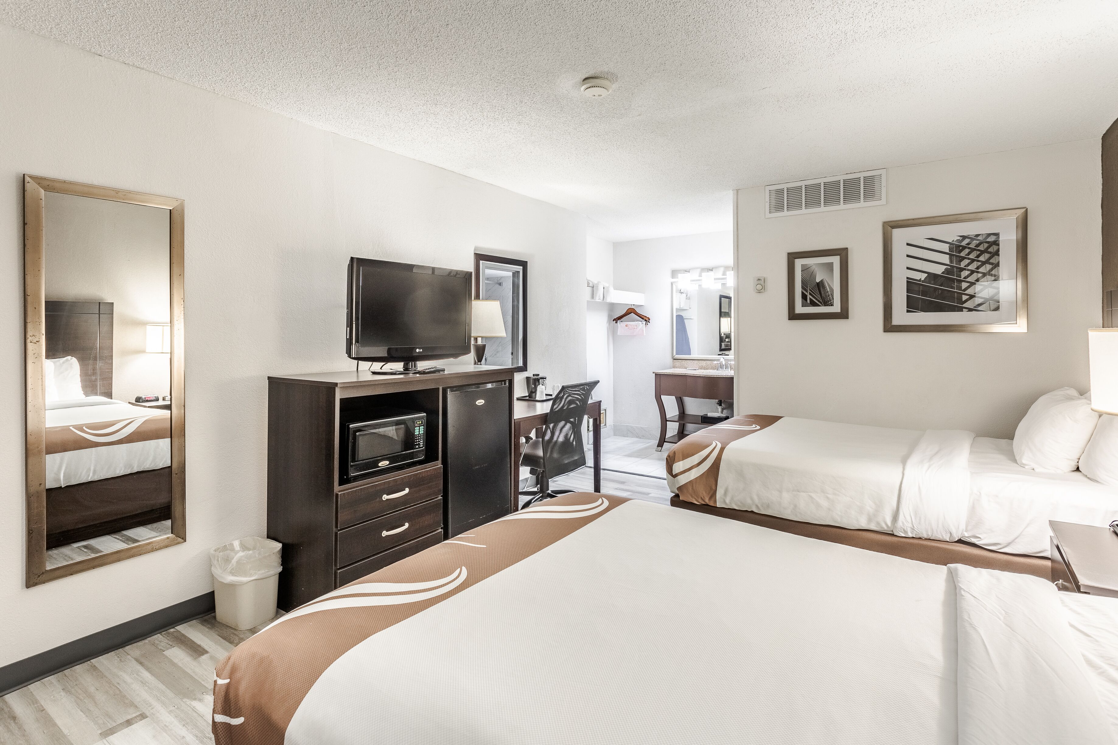 A hotel room with two beds, a desk with a computer, a television, and a mirror.