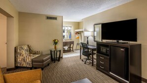 A hotel room with a sofa, a chair, a TV, a desk, and a minibar. - Quality Inn University (Lansing)