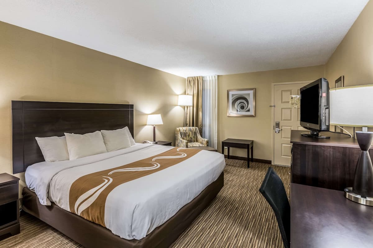 Una habitación de hotel con una cama grande, mesitas de noche, un escritorio, una silla, un televisor y una puerta.