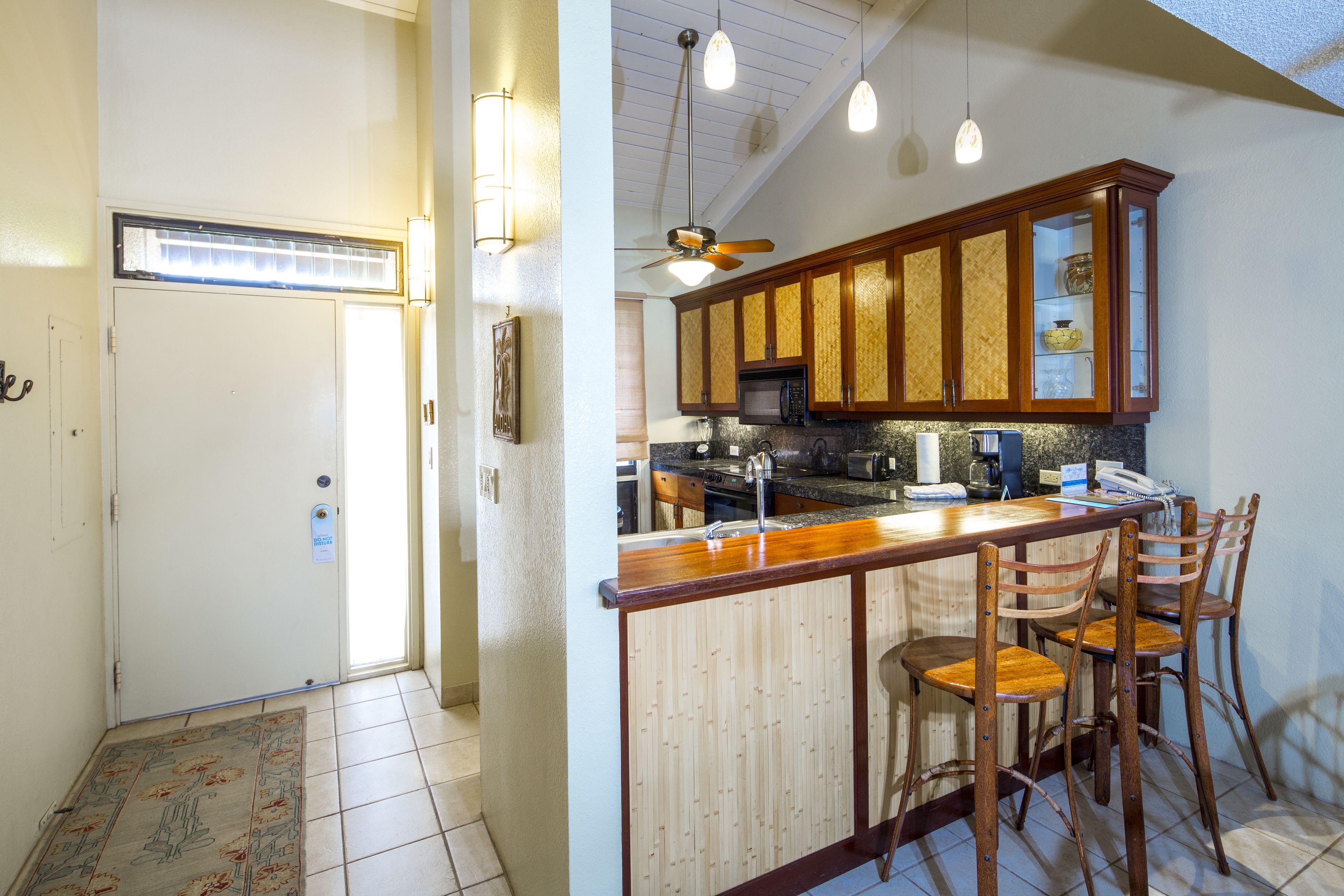 A kitchen with wooden cabinets, a microwave, and a bar area with chairs.