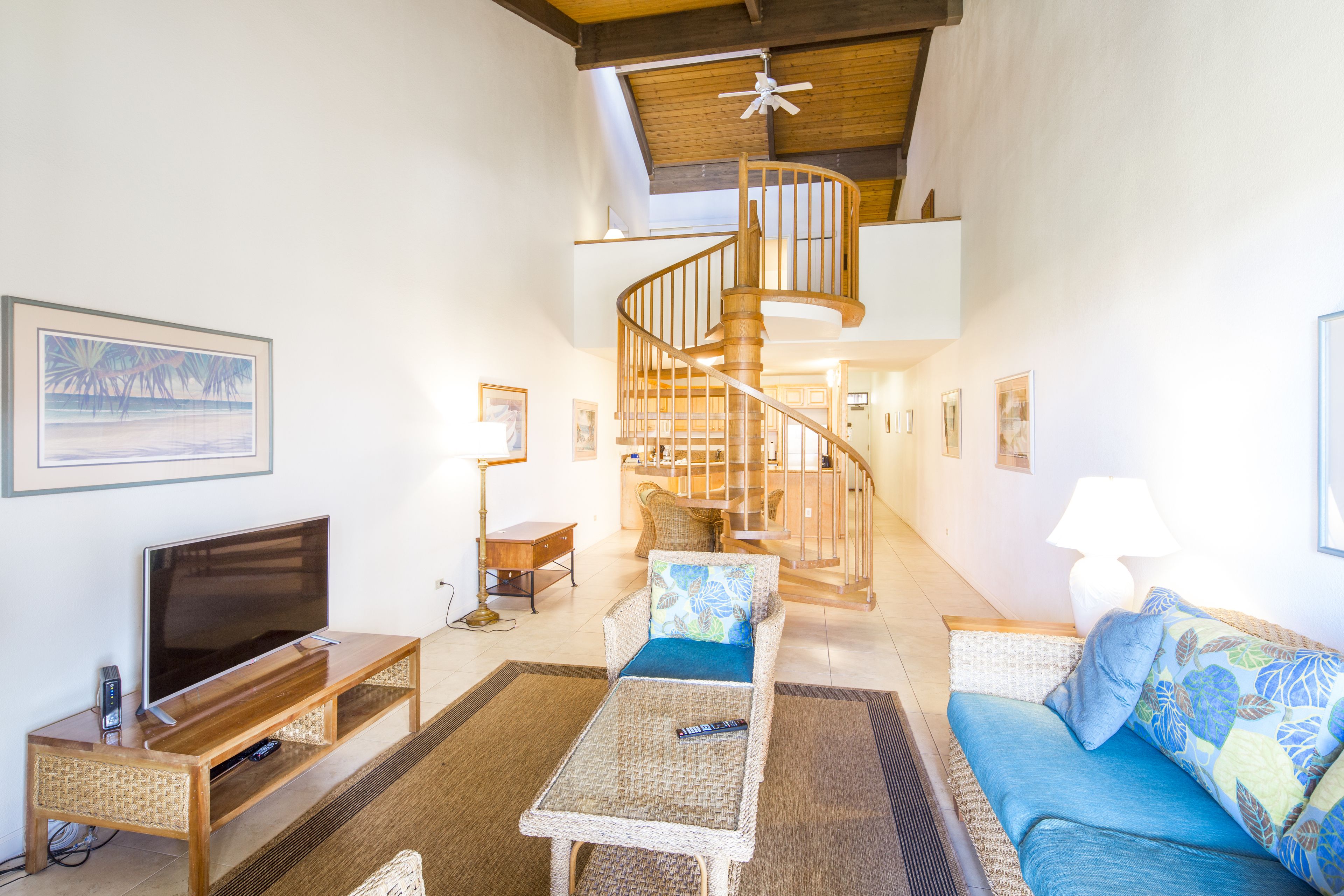 Ein geräumiges Wohnzimmer mit einer Holzeinbauwand, einer blauen Sofaausstattung, einem Couchtisch und einer Wendeltreppe, die in ein Obergeschoss führt.