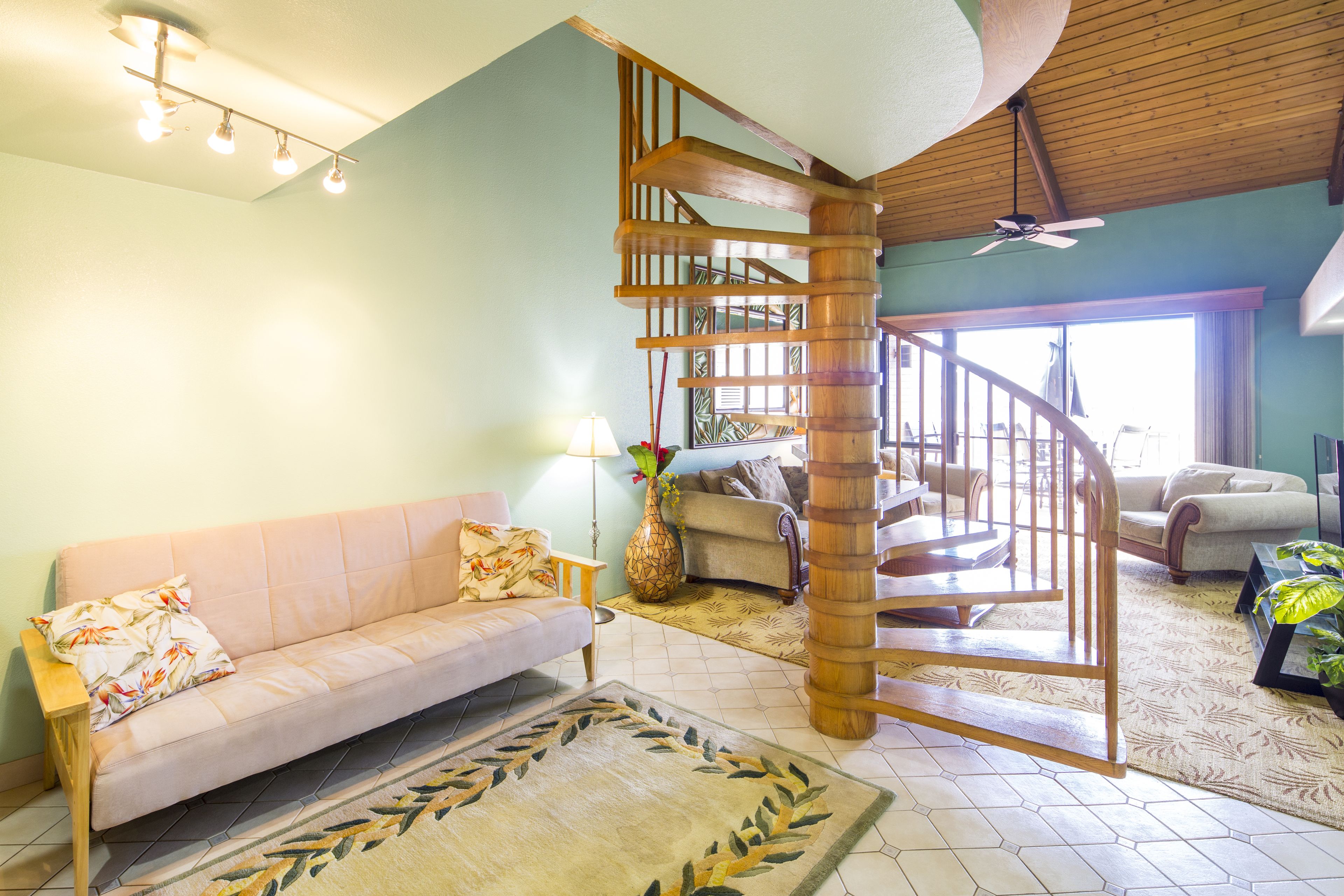 A spacious living area with a wooden staircase, a sofa, a coffee table, and a large window providing natural light.