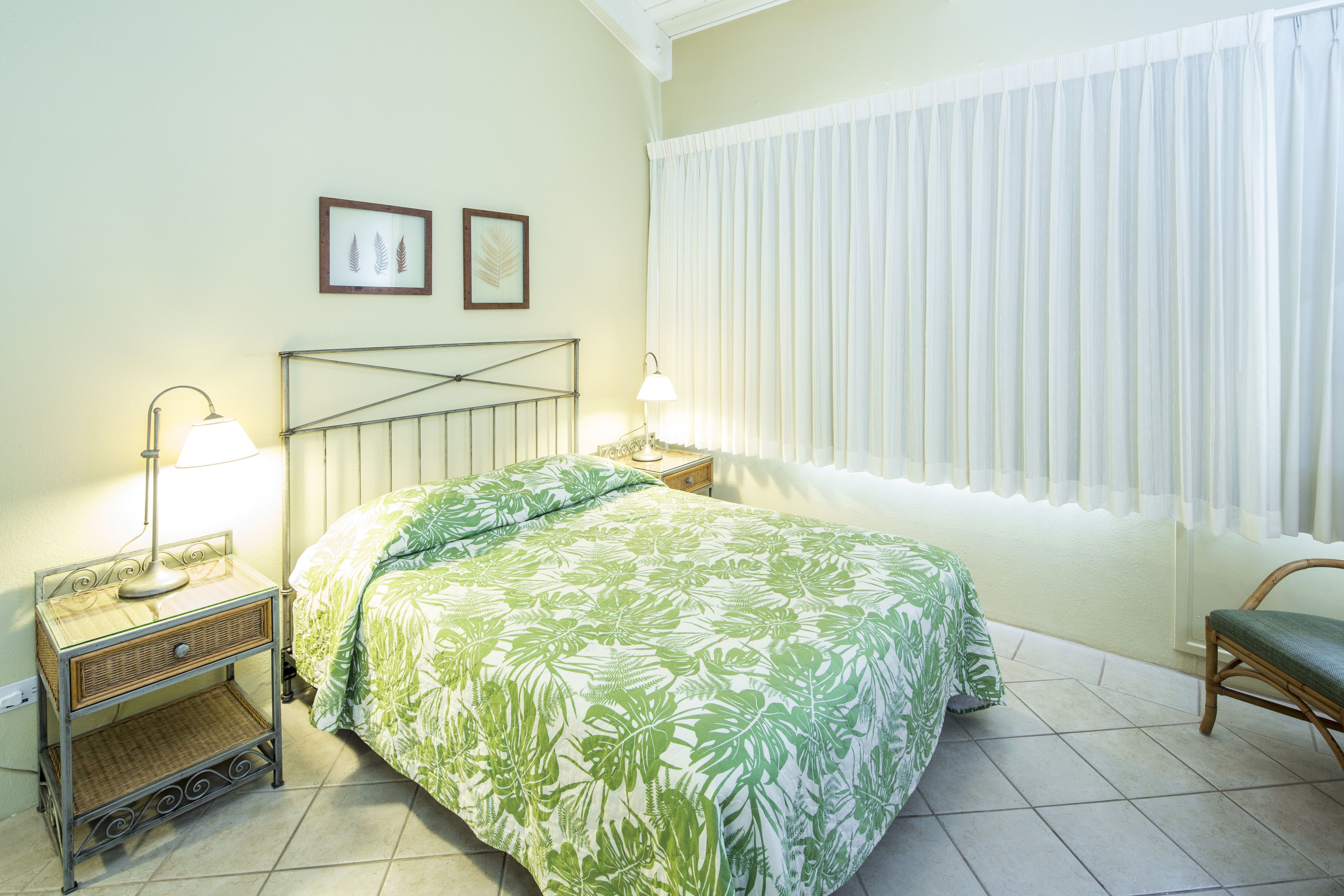 Un dormitorio con una cama, dos mesitas de noche, una lámpara, una silla y una ventana con cortinas.