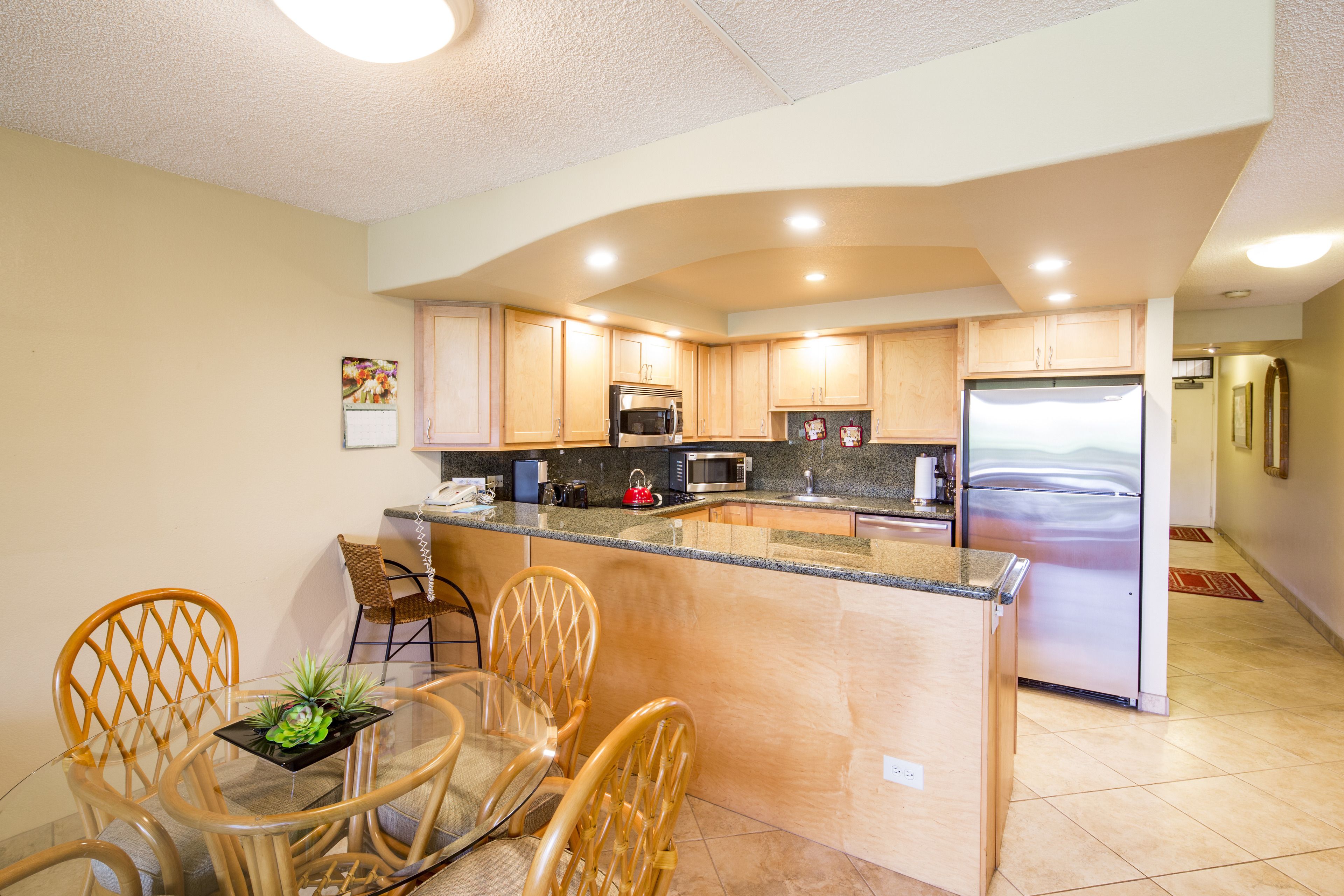A modern kitchen with wooden cabinets, a stainless steel refrigerator, and a glass dining table with chairs.