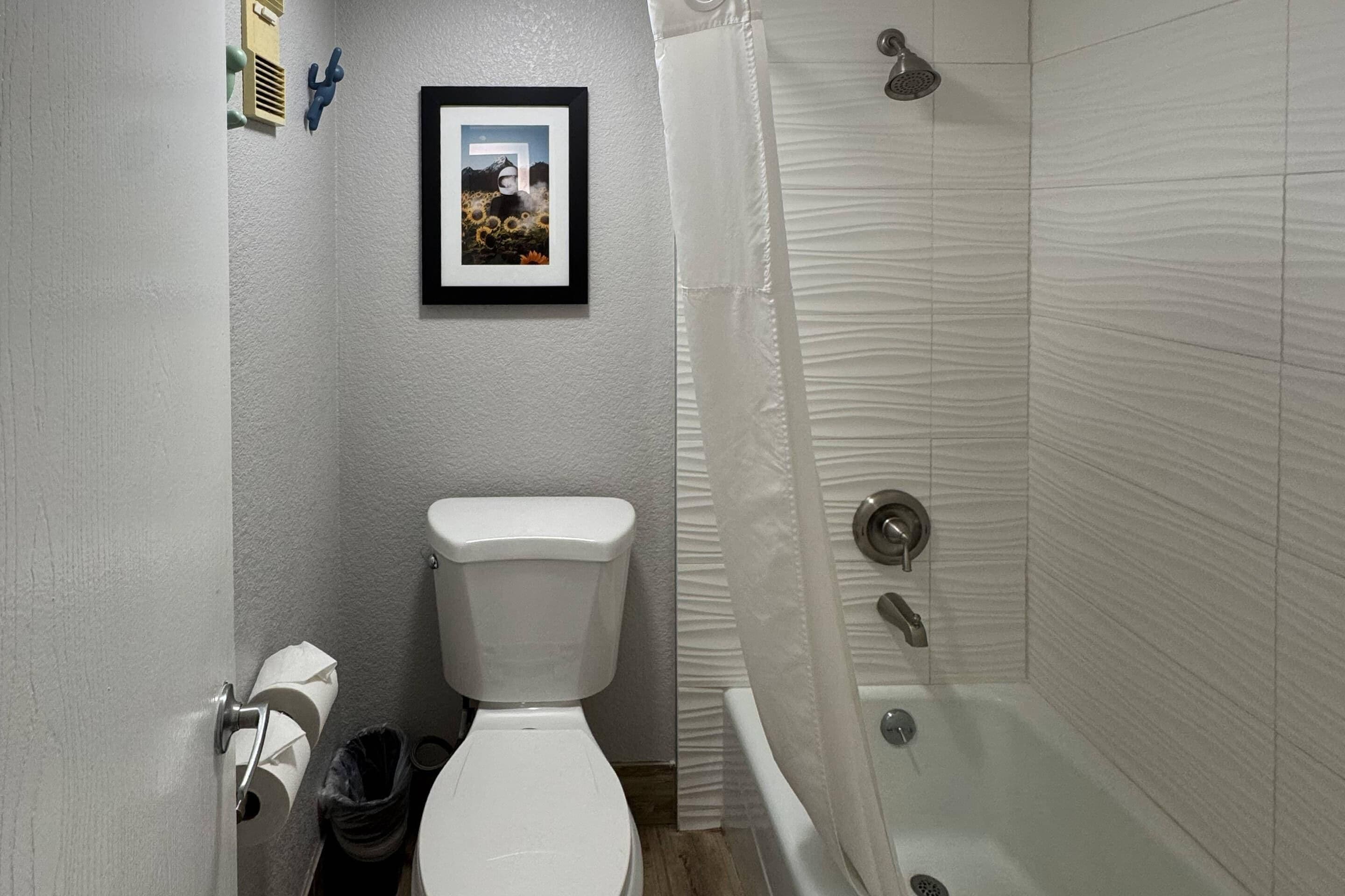 A bathroom with a toilet, a framed picture on the wall, a shower curtain, and a bathtub.