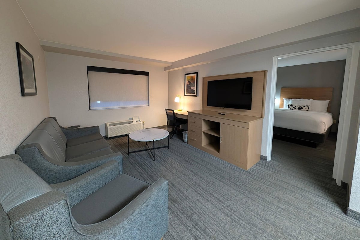 A hotel room with a sofa, a TV, a desk with a lamp, and a bed.
