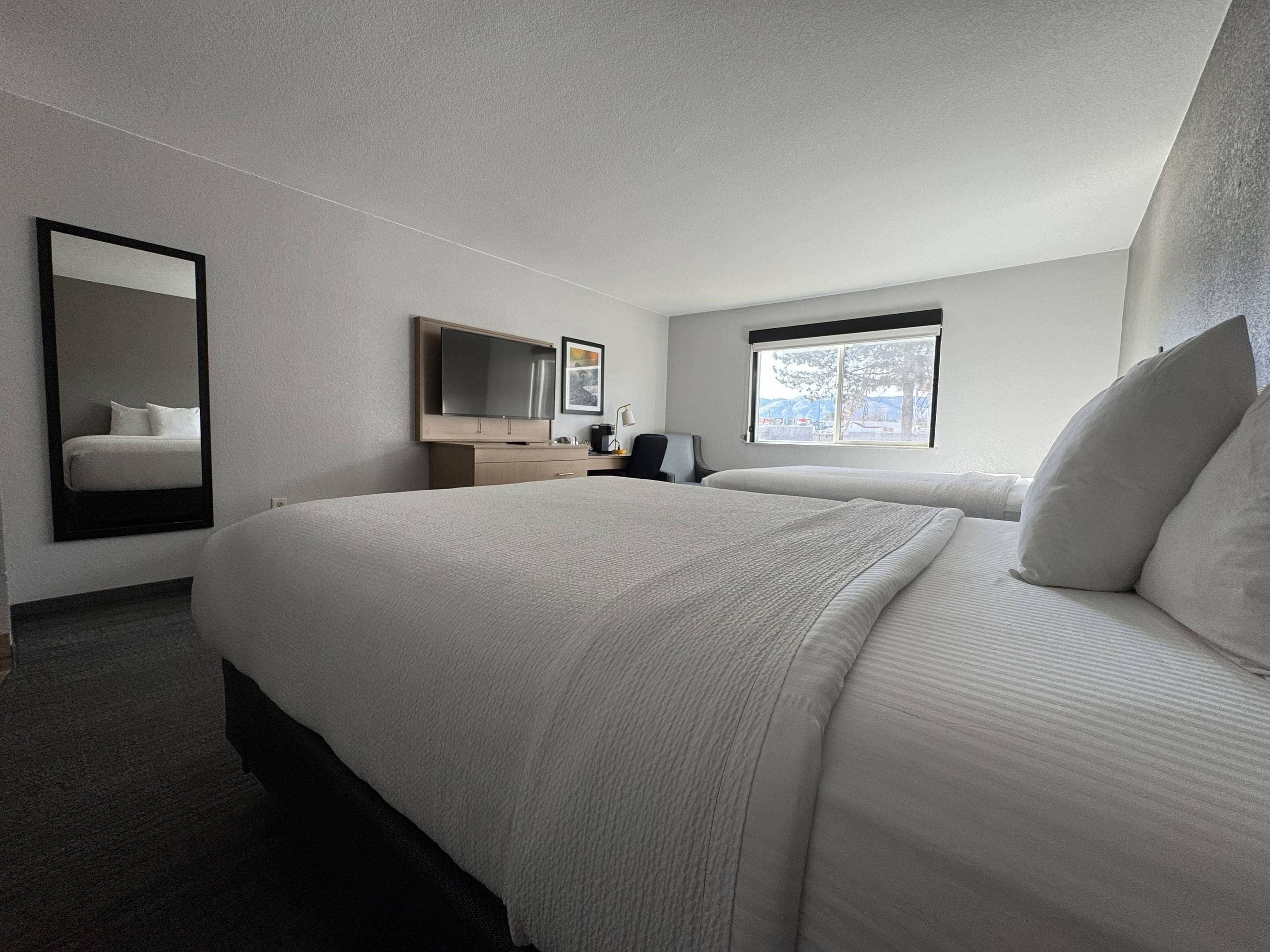 Una habitación de hotel con una cama grande, un escritorio, una silla, un televisor y una ventana con vistas.