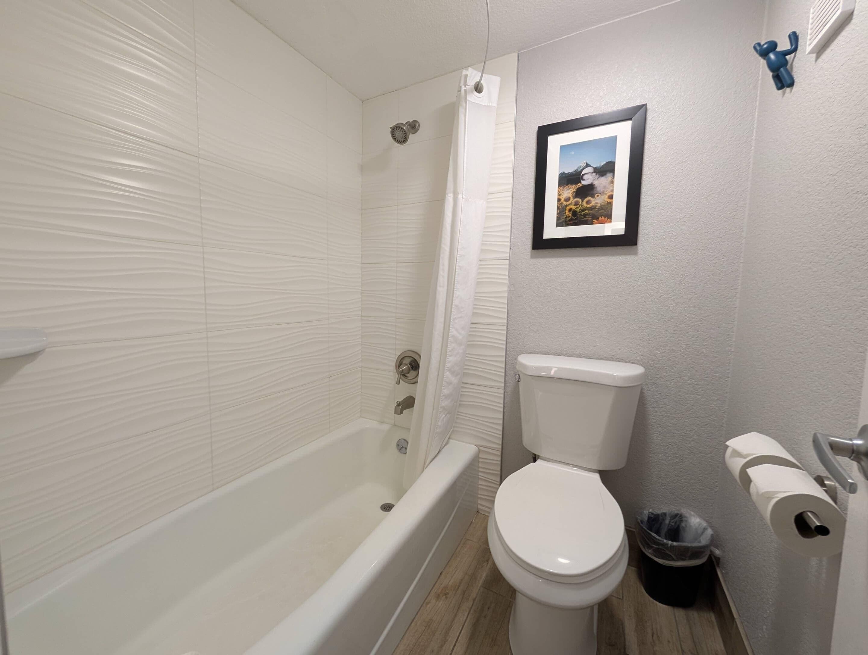 Et badeværelse med badekar, toilet og et billede i ramme på væggen.