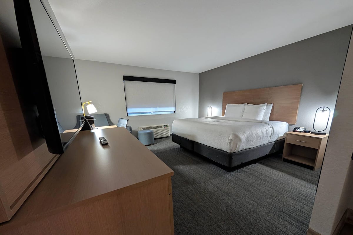 A hotel room with a bed, bedside table, lamp, and a desk with a chair.