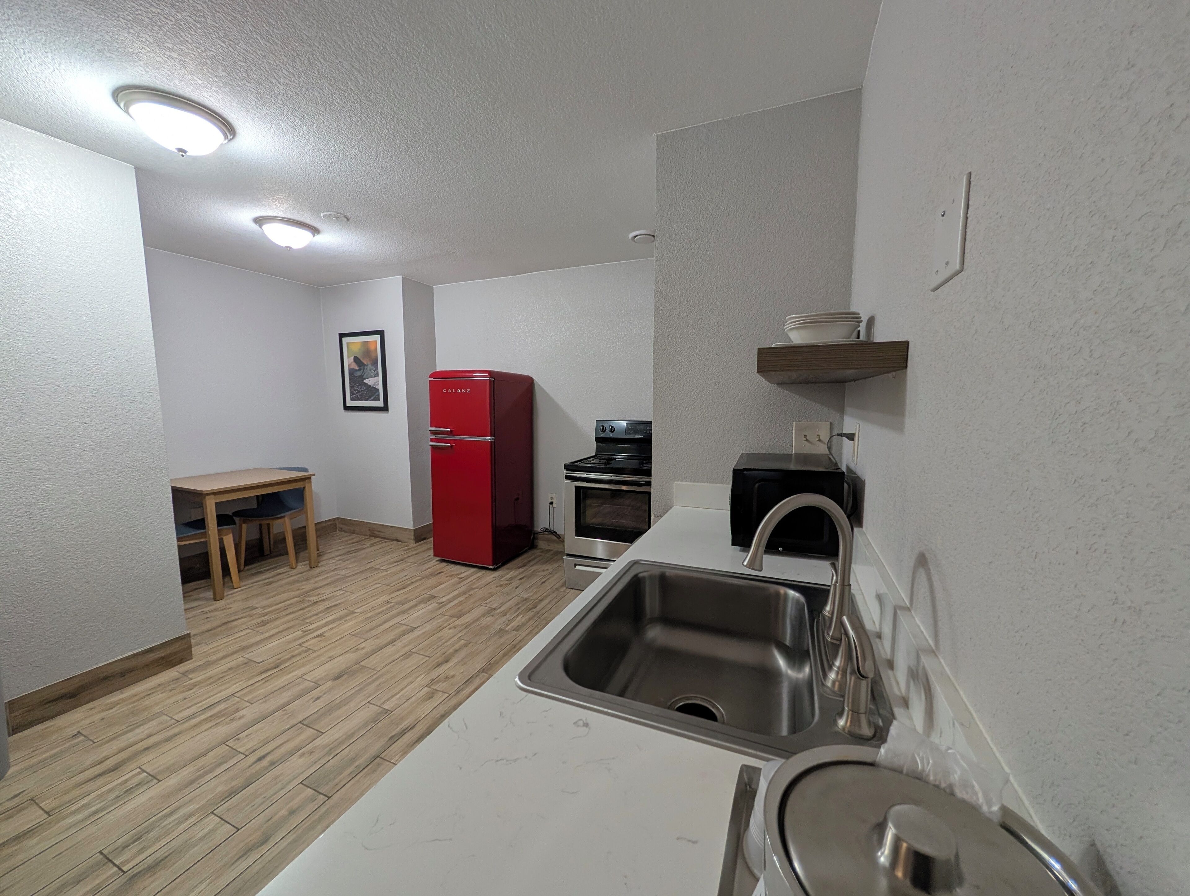 Eine kleine Küche mit Spüle, einem roten Kühlschrank, einem Tisch und einem Toaster.