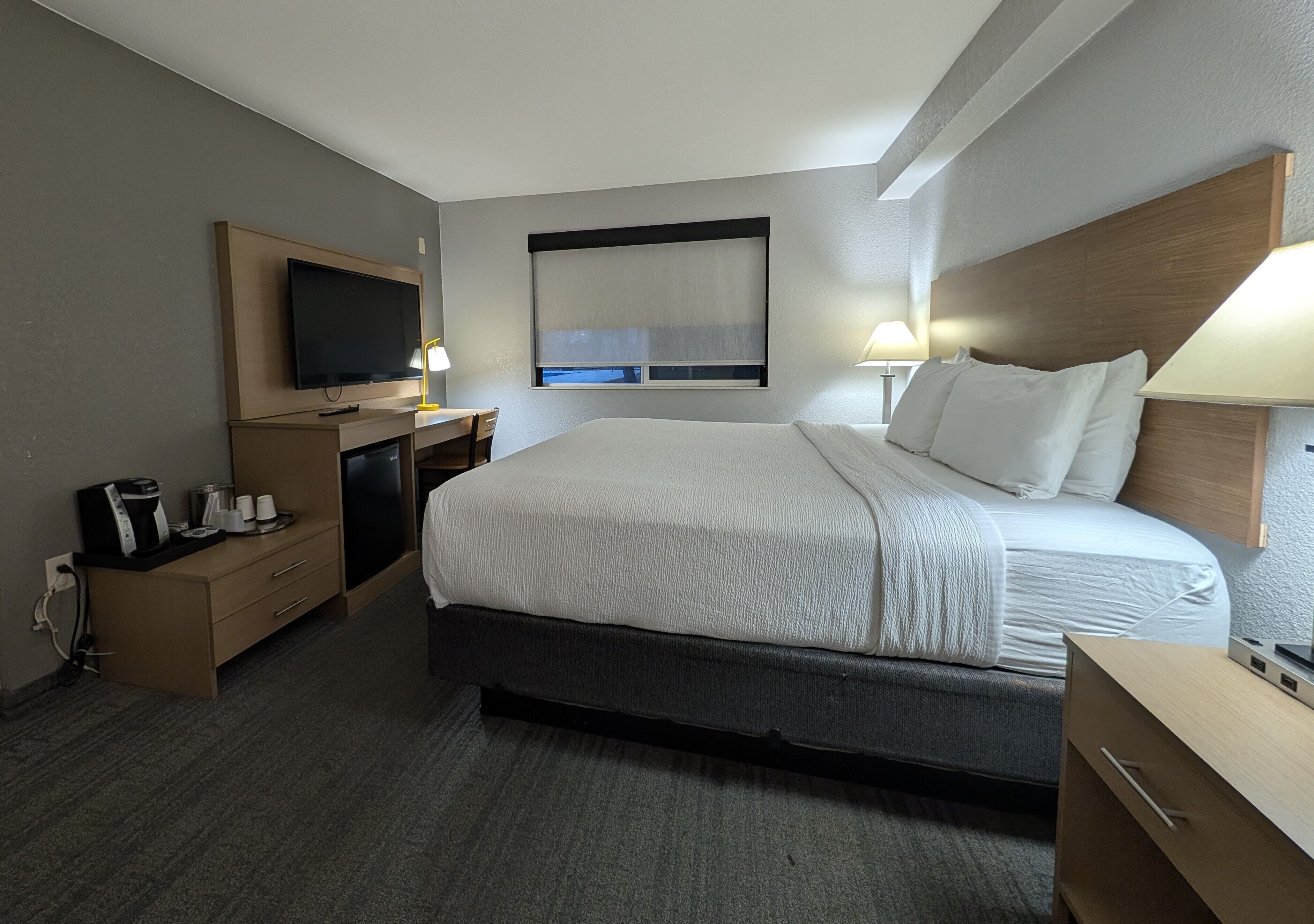 Une chambre d’hôtel avec un grand lit, des tables de chevet, une télévision et une fenêtre avec des stores.