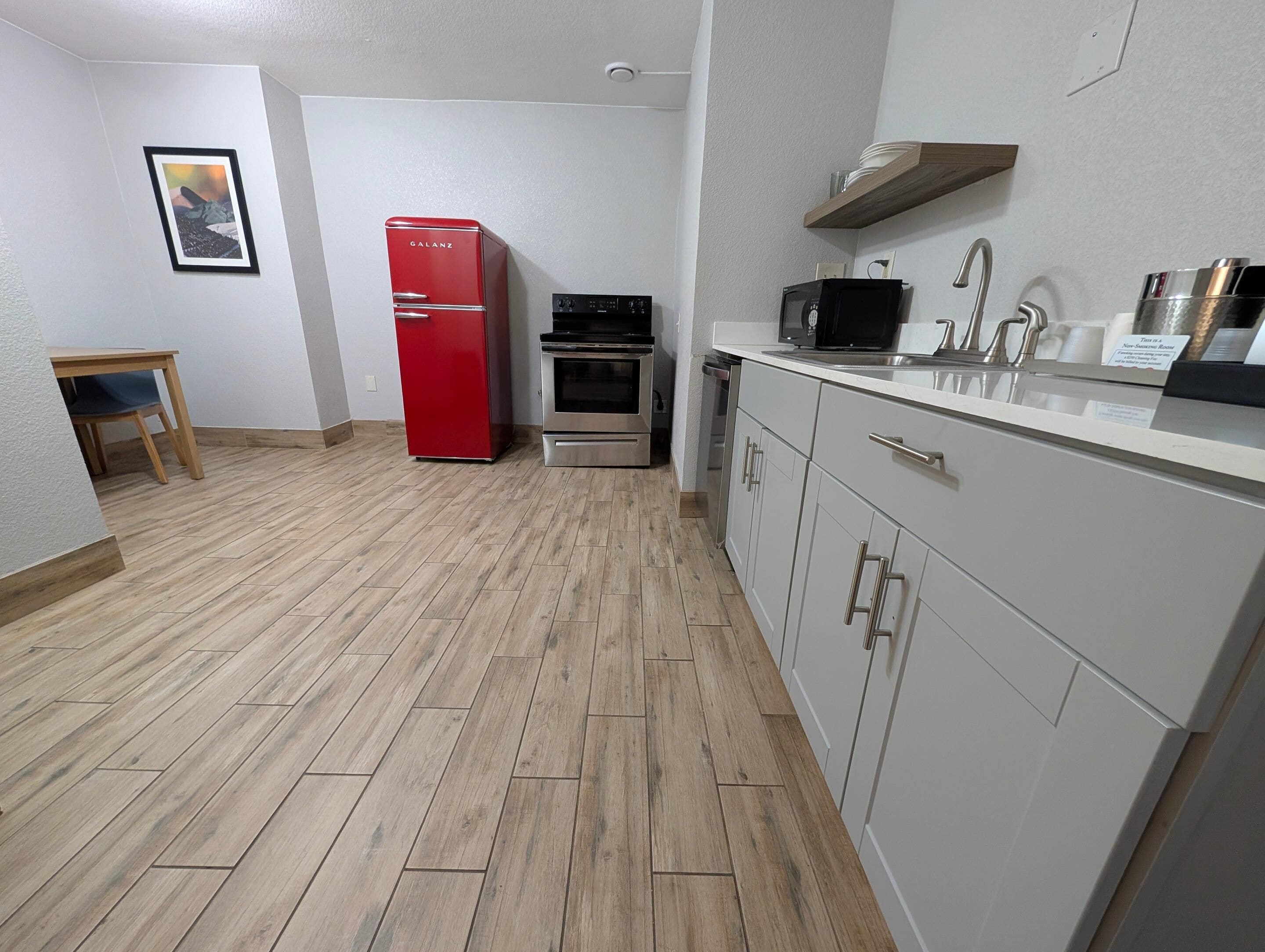 A compact kitchen with a red refrigerator, a microwave, an oven, and a sink.