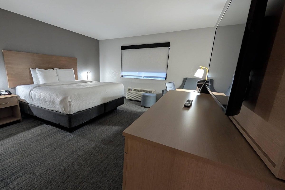 A hotel room with a bed, bedside table, lamp, desk, and a large mirror.