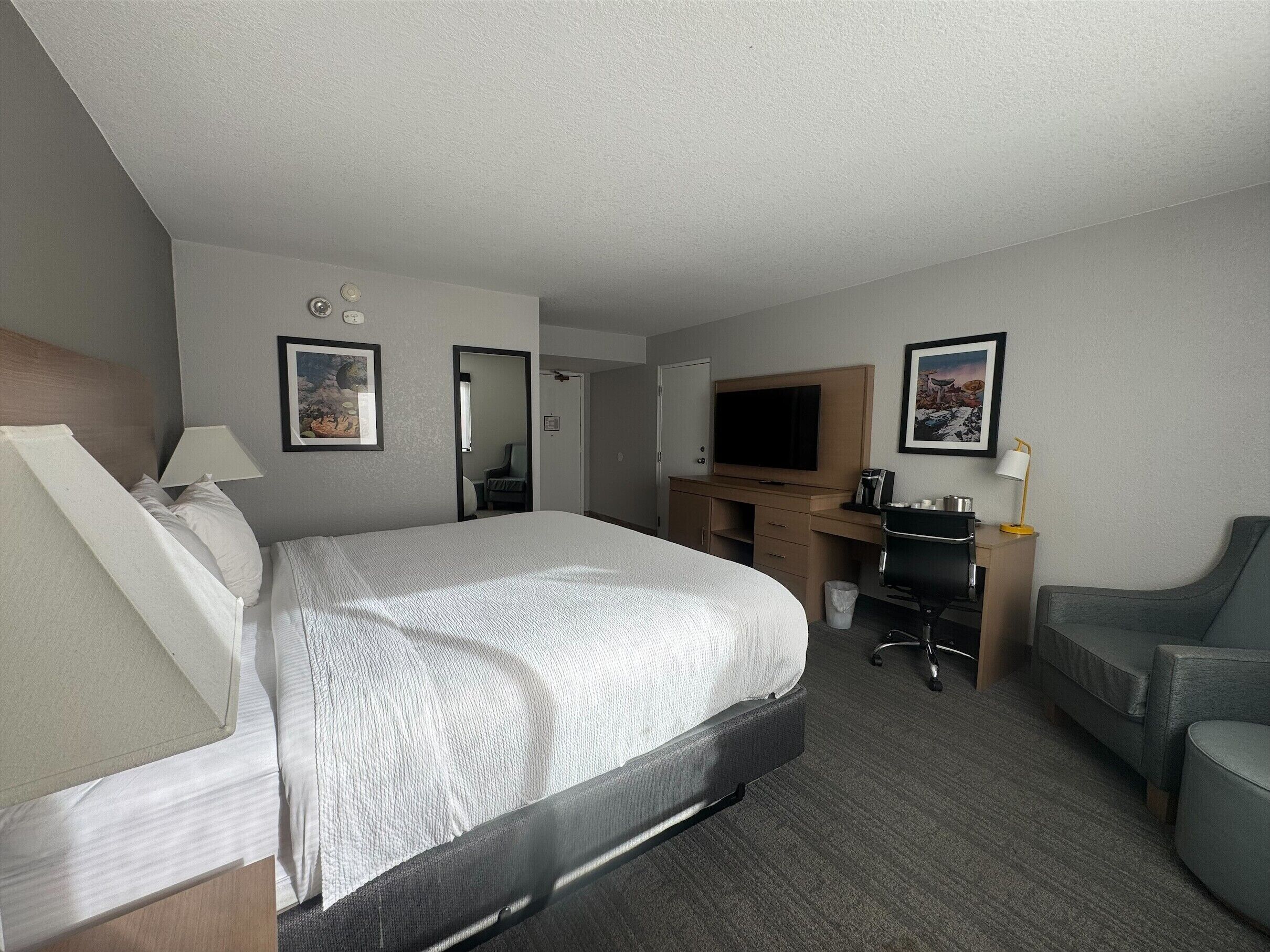A hotel room with a bed, desk, chair, TV, and a small table.