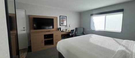 A hotel room with a bed, a TV, a desk with a chair, and a window.