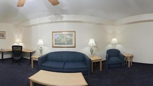 A hotel room with a blue sofa, a small table, two lamps, a chair, and a desk with a lamp. - Holiday Inn Express Fayetteville- Univ of AR Area by IHG (Fayetteville)