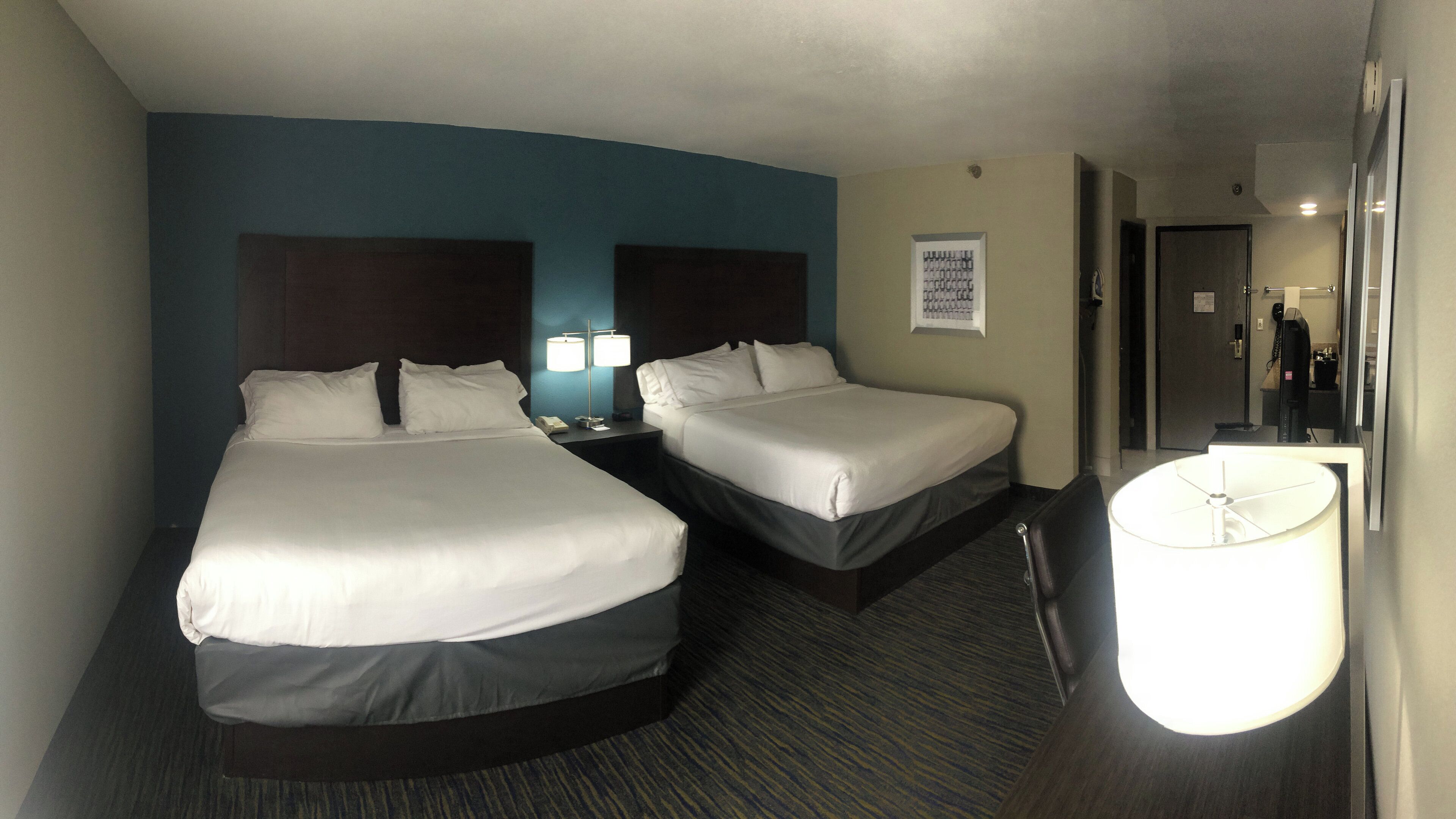 A hotel room with two beds, a nightstand, a lamp, and a desk with a computer.