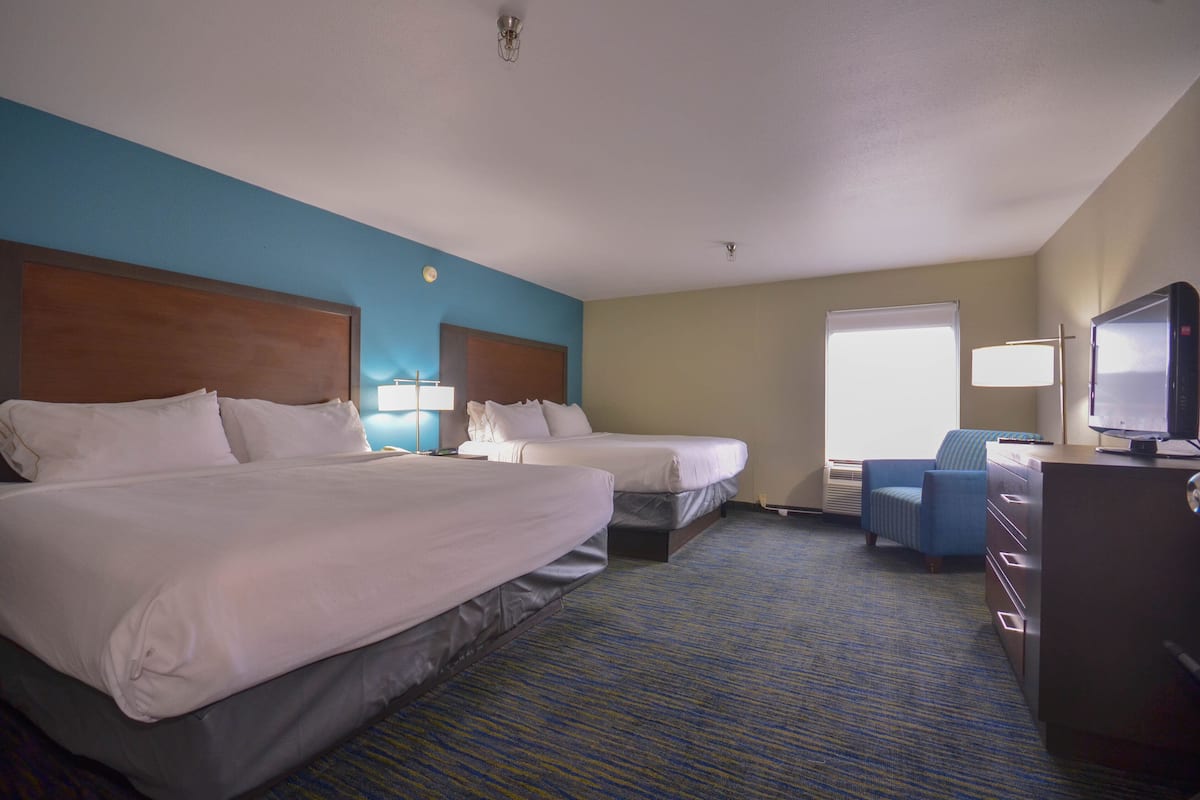 A hotel room with two beds, a desk, a chair, and a television.