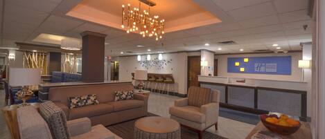 A hotel lobby with a reception desk, seating area, and a decorative ceiling light.
