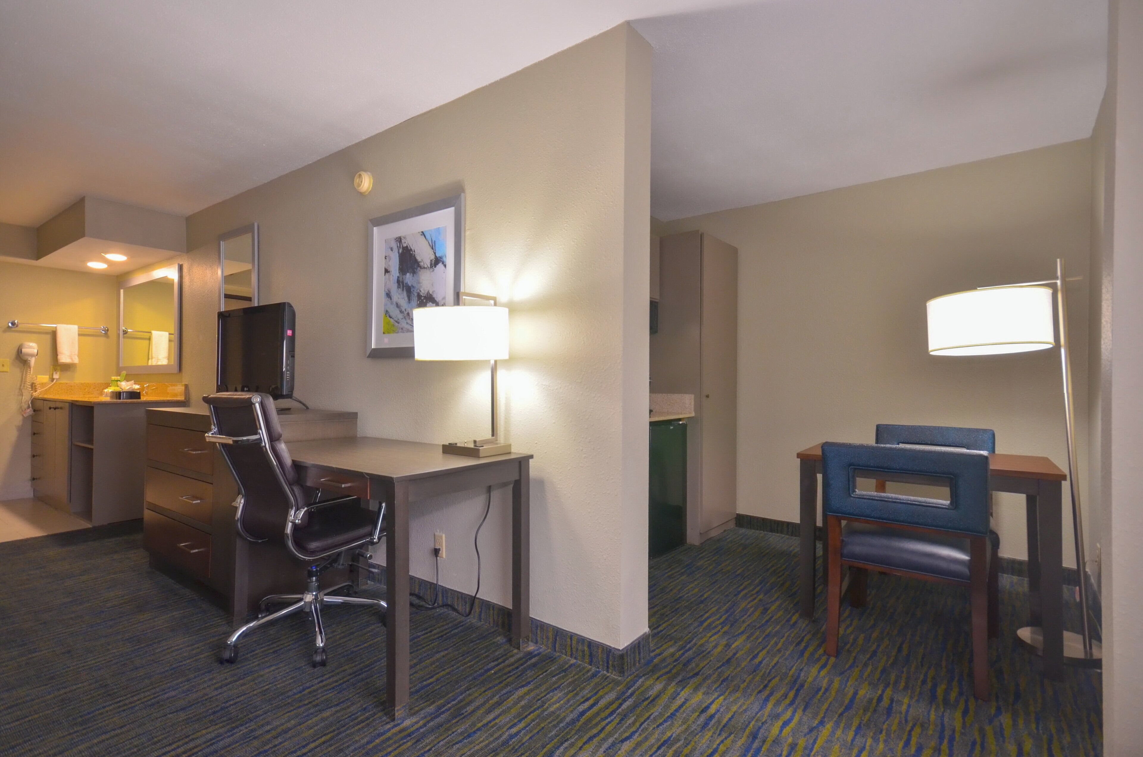 A hotel room with a desk, chair, and a bed.