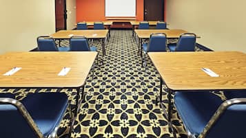 Un salón de conferencias con piso alfombrado, varias mesas y sillas dispuestas para reuniones.