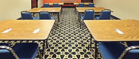 Un salón de conferencias con piso alfombrado, varias mesas y sillas dispuestas para reuniones.