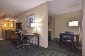 A hotel room with a desk, two chairs, a lamp, a mirror, a television, and a carpeted floor. - Holiday Inn Express Fayetteville- Univ of AR Area by IHG (Fayetteville)