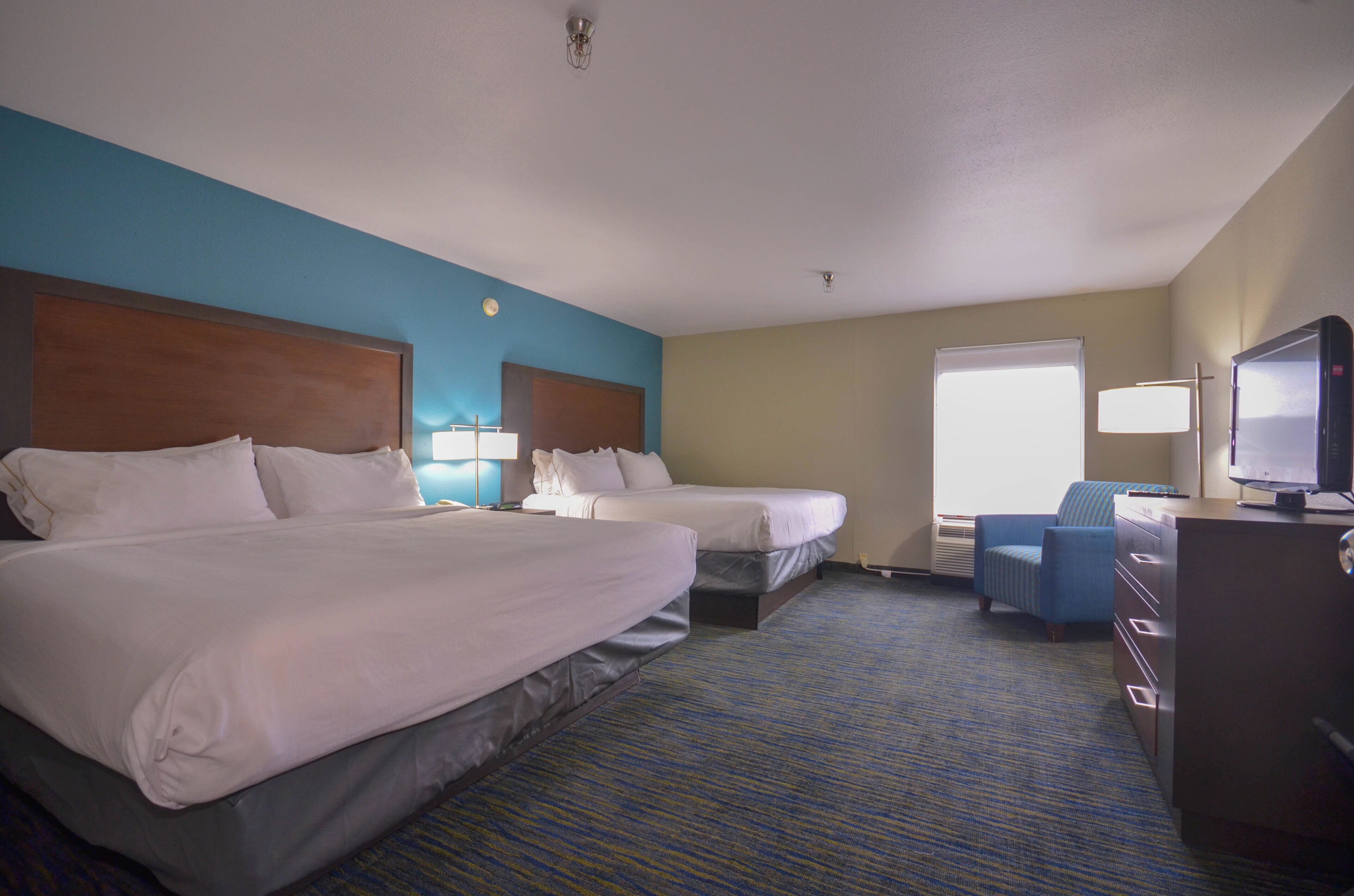 Quarto de hotel com duas camas, uma escrivaninha, uma cadeira e uma televisão.